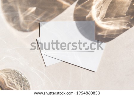 Still life scene with glasses on beige background in sunlight and blank business, greeting card, invitation mockup. Long harsh shadows. Flat lay, top view.