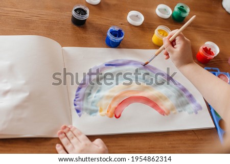 Close-up of a little girl paints a rainbow at the table in the living room. Love, peace and happy childhood concept