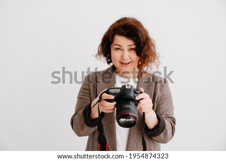 happy brunette woman with curly hair in a T-shirt and a checkered jacket on a white background looks at pictures on camera display. photographer's job or favorite hobby