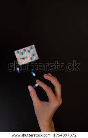 The girl holds the pill with her fingers in close-up. A blister with pills in the background out of focus. on a black background