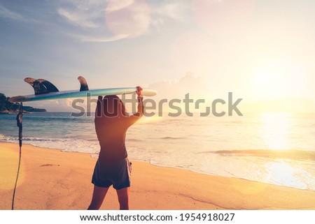 Woman hold surfboard standing at tropical sunset beach background. Summer vacation and sport adventrue concept. Vintage tone filter effect color style.