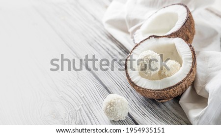Two halves of coconut and coconut sweets on a wooden table .  Coconuts on a white napkin . Handmade coconut sweets with a copy space  .  Horizontal orientation picture with a coconut .