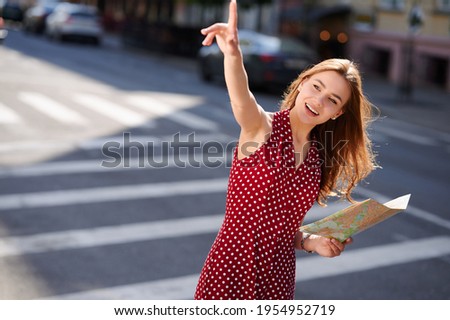 Young woman traveler holding a paper map of the city in her hands and calling someone on the street in summer