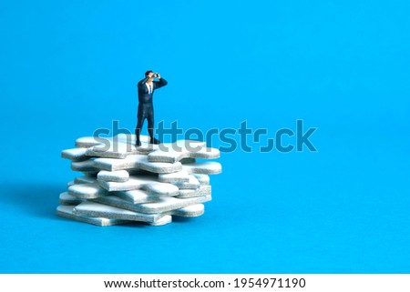 Businessmen standing above jigsaw puzzle piece stack using binoculars above wooden table. Miniature tiny people toys photography. isolated on blue background.