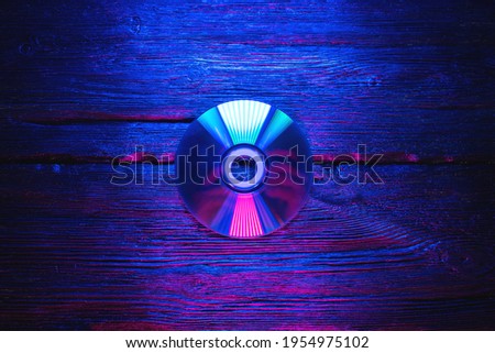 Cd disk in the neon lights on the black flat lay table background.