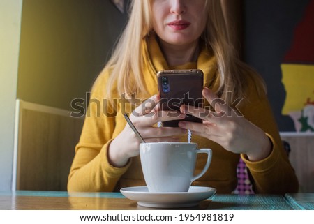 Blogger girl sits in a cafe and shoots a cappuccino foam on the smartphone. Work in social networks, video blogs and photo blogs. Concept for internet content creation and food photography.