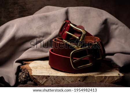Red and orange belt with gold buckles lie on a wooden cut on a brown background close-up