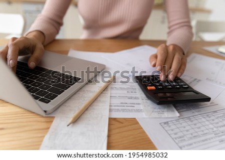 Bookkeeping requires accuracy. Young woman hands typing on computer and digital calculator keyboards preparing electronic payments of utility bills counting taxes sum balancing accounts. Close up view Royalty-Free Stock Photo #1954985032
