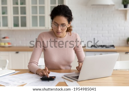 Focused millennial latin woman auditor accountant manage paperwork at home office do calculation use pc to provide transaction. Young female student check tuition fee sum before pay in e-bank service Royalty-Free Stock Photo #1954985041