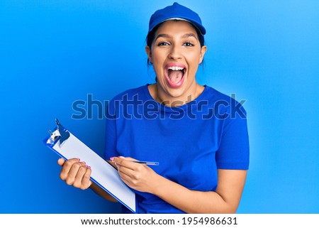 Beautiful brunette woman wearing courier uniform holding clipboard smiling and laughing hard out loud because funny crazy joke. 