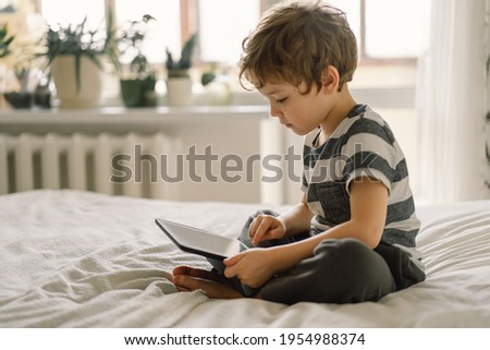 Little Boy with a tablet in the room. The boy play game on the tablet. Technology concept. Child with a gadget
