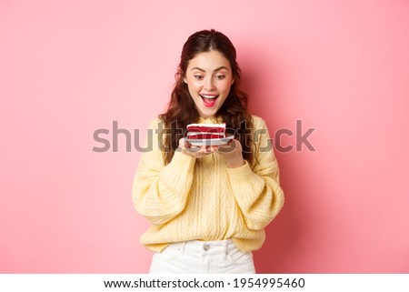 Celebration and holidays. Happy birthday girl stares at delicious bday cake dessert and smiles, stands against pink background