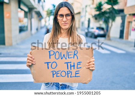 Young caucasian woman with relaxed expression holding power to the people banner cardboard at the city.