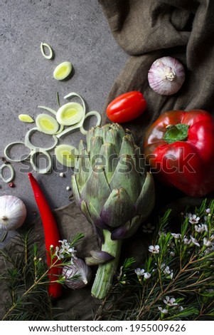 Vegetarian meal ingredients top view photo. Leek, zucchini, artichoke, pepper, garlic and herbs on gray background. Fresh seasonal vegetables on a table.