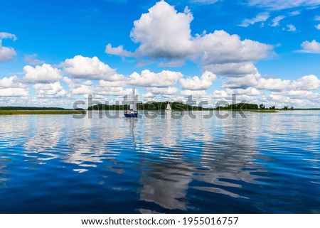 Sailing yacht in the lake with gloomy sky before the rain. Yacht sailing on the lake against a blue sky with clouds. Sailboat vacations on a lake. Royalty-Free Stock Photo #1955016757