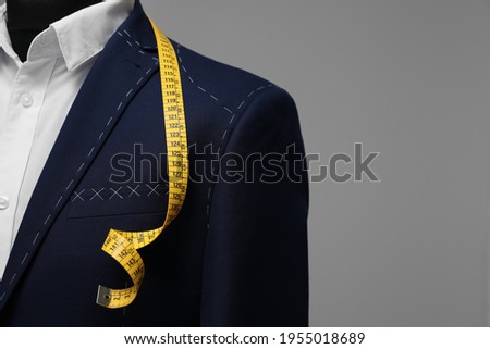 Semi-ready jacket with tailor's measuring tape on mannequin against grey background, closeup. Space for text Royalty-Free Stock Photo #1955018689