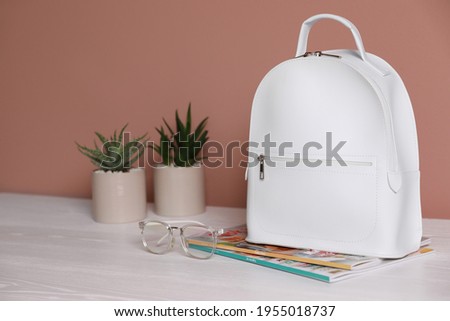 Stylish urban backpack, glasses and magazines on white wooden table