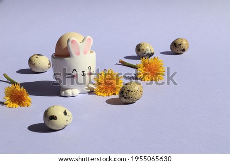 Egg in a rabbit stand with quail eggs and dandelion flowers on a blue background, space for text