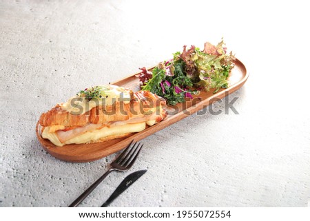 Croissant with cheese inside and in the top, and lettuce in brown wooden plate on white background 