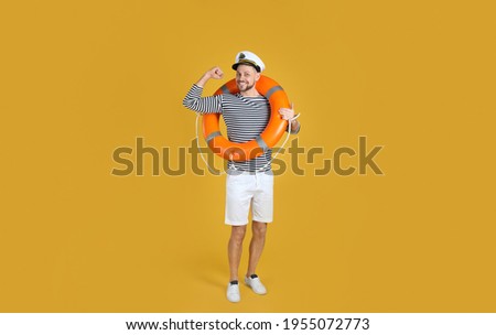 Sailor with orange ring buoy showing biceps on yellow background Royalty-Free Stock Photo #1955072773