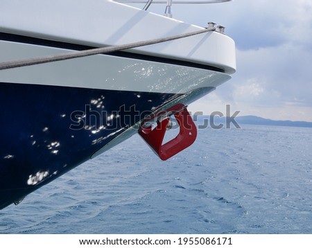 Metal rigging on a blue yacht. Red anchor in the bow of a moored yacht against the background of the sky and the sea surface on a sunny summer day. Metal rigging on a blue yacht.