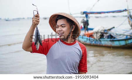 Happy young fisherman on the beach holding his catch fish and shows in front of his boat