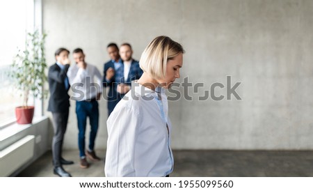 Workplace Bullying And Sexism. Male Colleagues Whispering Behind Back Of Unhappy Business Lady In Office. Victimization At Work. Female Discrimination Corporate Problem. Selective Focus, Panorama Royalty-Free Stock Photo #1955099560