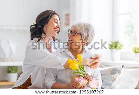 Beautiful young woman and her mother with flowers tulips in hands at home.  