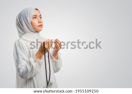 Portrait of Asian Muslim woman prays to God, praying gesture hands raised up and holding prayer beads, against a white background