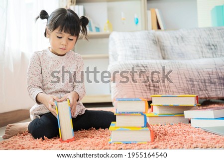 A little cute girl reading a picture book a book sitting on the floor
