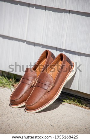 A pair of brown leather loafers for men against a modern wooden wall in the sun for an outdoor fashion photoshoot of footwear.