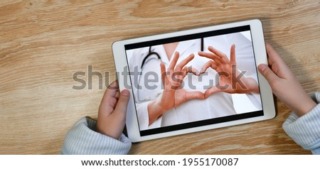 Gesture heart from folded hands, a message of love and care from the doctor to the patient, through the screen of the gadget, in the hands of a terry robe. Telemedicine. Royalty-Free Stock Photo #1955170087