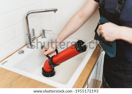 Plumber unclogging kitchen sink with professional force pump cleaner. Royalty-Free Stock Photo #1955172193