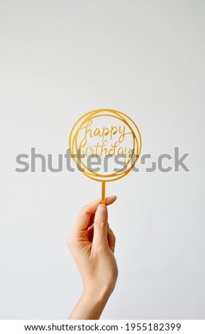 Cropped hand holding round golden acrylic Happy Birthday Party Sign in white background