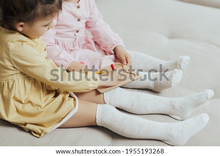 Two cute little girls sitting on the couch and drawing on wooden board with felt pen. Early education concept.