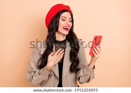 Photo portrait of laughing girl holding phone in one hand isolated on pastel beige colored background