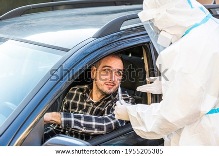 Man sitting in car, waiting for medical worker to perform drive-thru COVID-19 test, taking nasal swab sample through car window, PCR diagnostic for Coronavirus, doctor in PPE holding test kit.