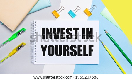 On a gray and blue background are stationery of yellow-green color, a notebook with the text INVEST IN YOURSELF. Flat lay.