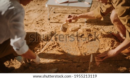 Archaeological Digging Site: Two Great Archeologists Work on Excavation Site, Carefully Cleaning, Lifting Newly Discovered Ancient Civilization Cultural Artifact, Historic Clay Tablet. Focus on Hands Royalty-Free Stock Photo #1955213119