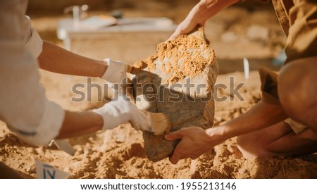 Archeological Digging Site: Two Great Archeologists Work on Excavation Site, Carefully Cleaning, Holding Newly Discovered Ancient Civilization Cultural Artifact, Historic Clay Tablet, Fossil Remains Royalty-Free Stock Photo #1955213146