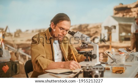 Archaeological Digging Site: Male Archeologist Doing Indigenous Culture Research, Discovers Ancient Civilization Historical Artifacts, Fossil Remains at Excavation Site, Study it Under Microscope Royalty-Free Stock Photo #1955213227