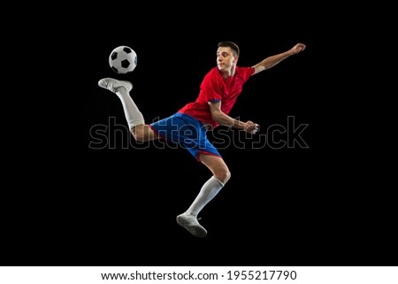 Young Caucasian soccer football player practicing isolated on black background.