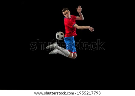 Young Caucasian soccer football player practicing isolated on black background.