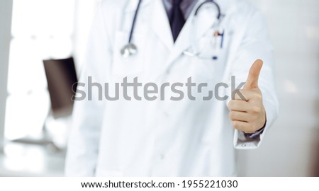 Unknown male doctor standing with thumbs up sign in clinic near his working place, closeup. Perfect medical service in hospital. Medicine and healthcare concept