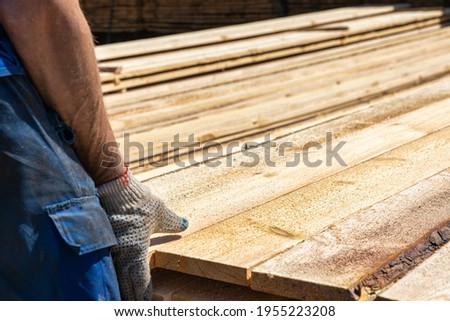 Industrial warehouse of a sawmill, an employee puts his hands on the finished products at the sawmill in the open air. Commercial background of the hand on the left side. Royalty-Free Stock Photo #1955223208