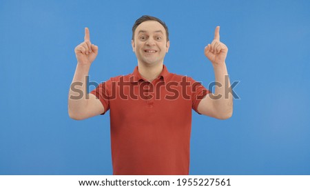Young fun happy young man points with two fingers in the ad space at the top of the screen.Indoor studio shot isolated on blue background. 