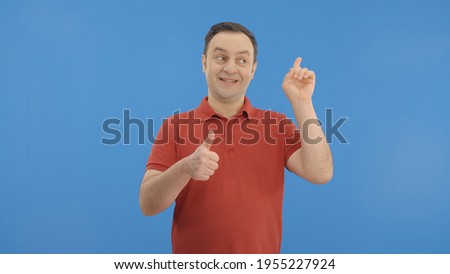 The young man points the ad space above him, after making a thumbs up sign. Show the ad space. Thumb up sign. Indoor studio shot isolated on blue background. 