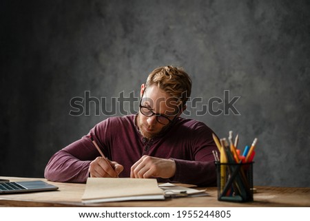 A man writing something in a diary while sitting at a table in the studio
