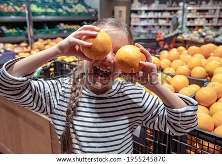 Cheerful little girl posing with oranges in a grocery store.