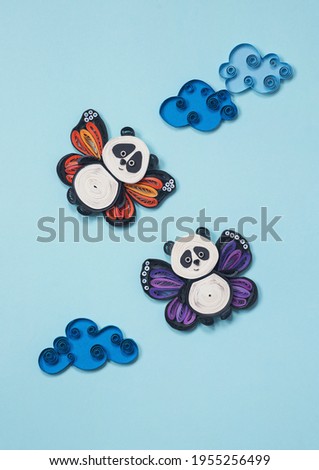 Happy cute panda flying in the sky between clouds. Two little pandas with butterfly wings. Happiness, dreaming and freedom concept. Hand made of paper quilling technique.
